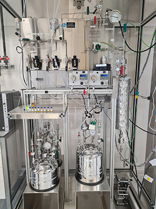 Advanced laboratory setup with interconnected stainless steel reactors, tubing, gauges, and analytical instruments for chemical processing